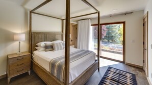 A four-poster canopy bed with a wooden frame, a nightstand with drawers, and a view of a garden through a glass door. - Sun Valley Condo w/ Furnished Patio: Near Skiing! (Sun Valley)
