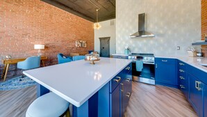 Une cuisine moderne avec des meubles bleus, un îlot central blanc et un mur en briques.