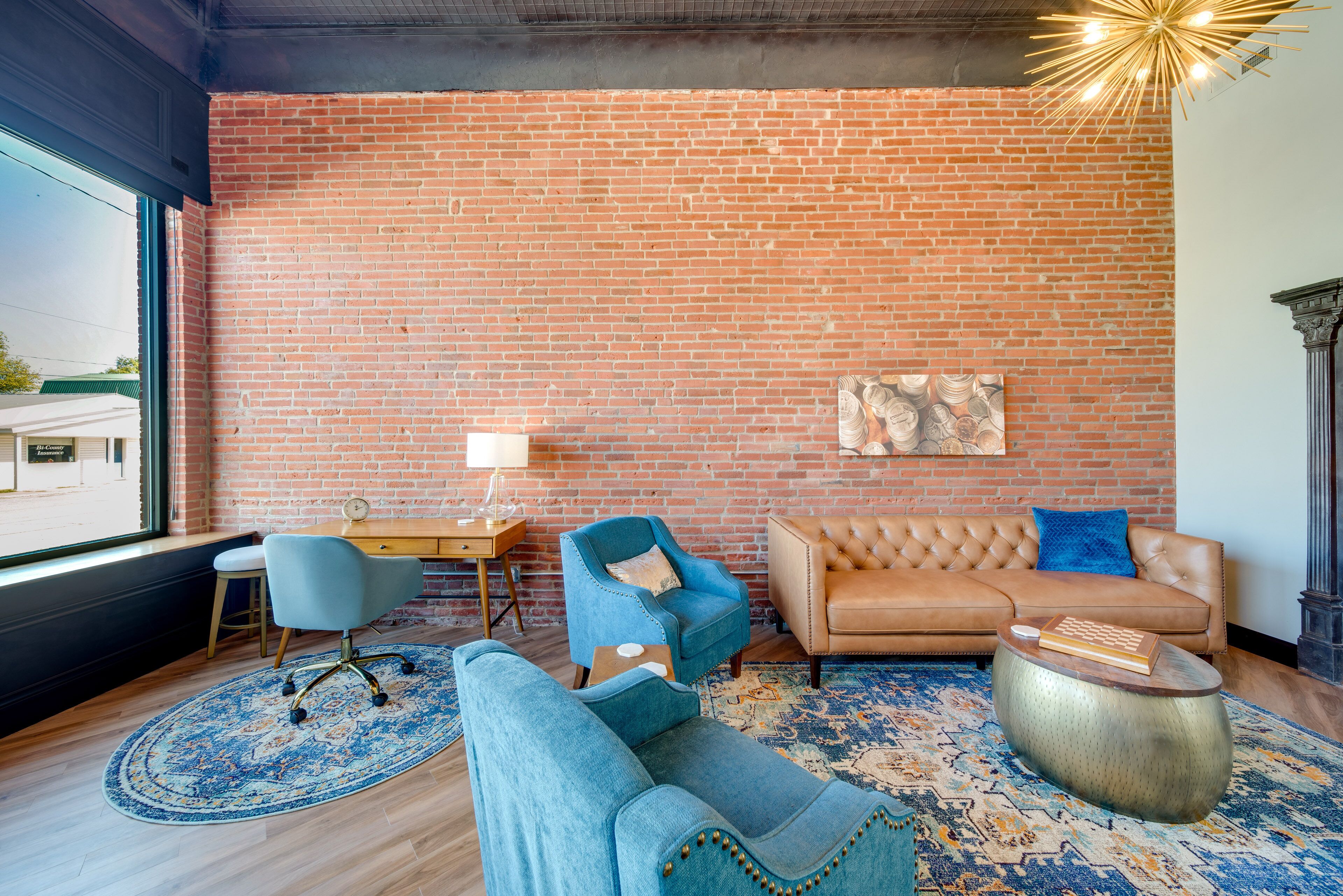 Una sala de estar moderna con pared de ladrillo, un sofá de cuero, un sillón azul, una mesa de centro redonda y un tapete estampado.