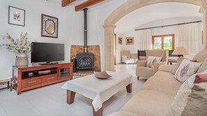 A living room with a TV, fireplace, sofa, and a stone wall. - Villa Ca Na Francisca - By Dream Villas Pollensa (Pollensa)