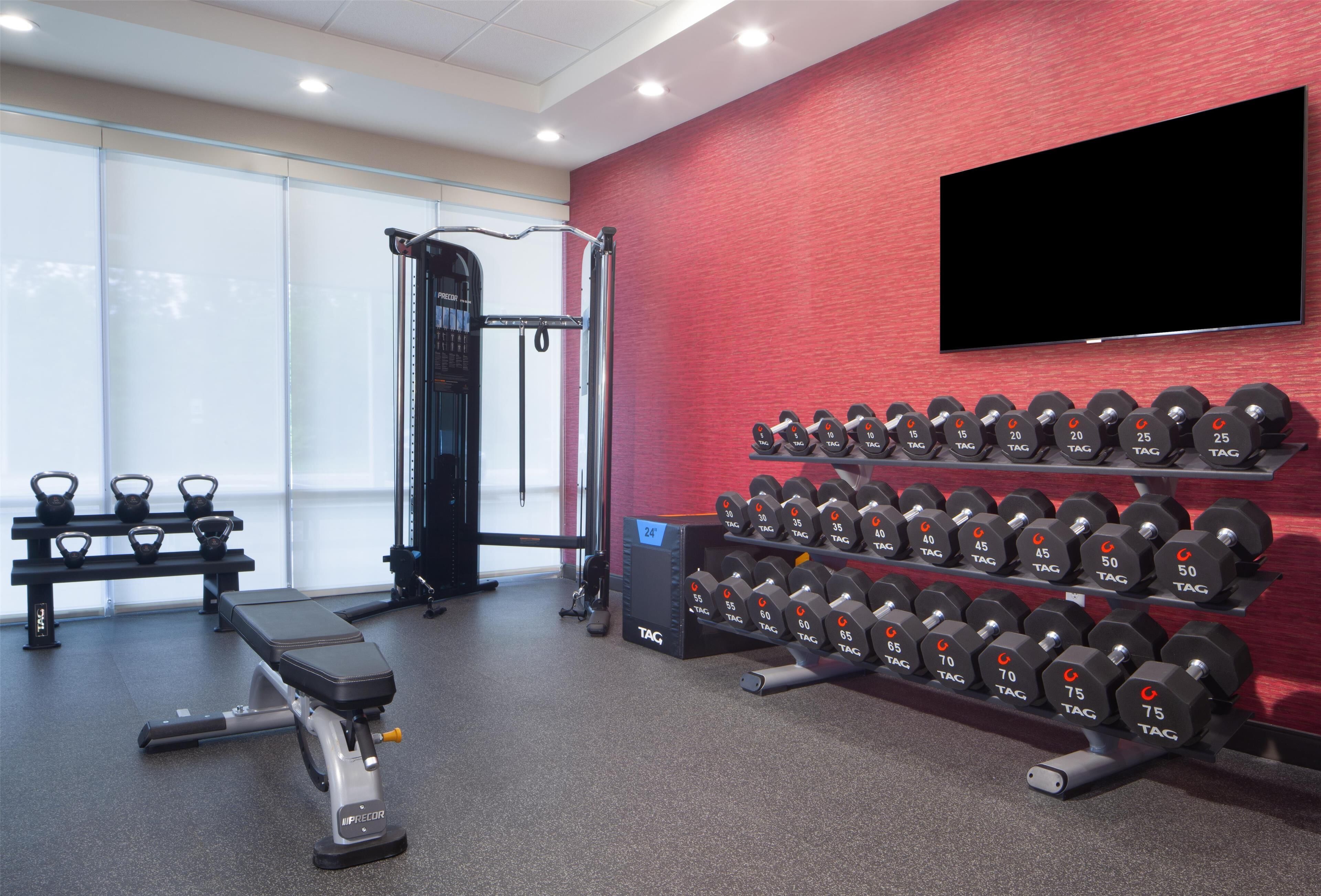 Un gimnasio con equipo de levantamiento de pesas, incluyendo mancuernas y bancos.
