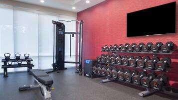 Un gimnasio con equipo de levantamiento de pesas, incluyendo mancuernas y bancos.