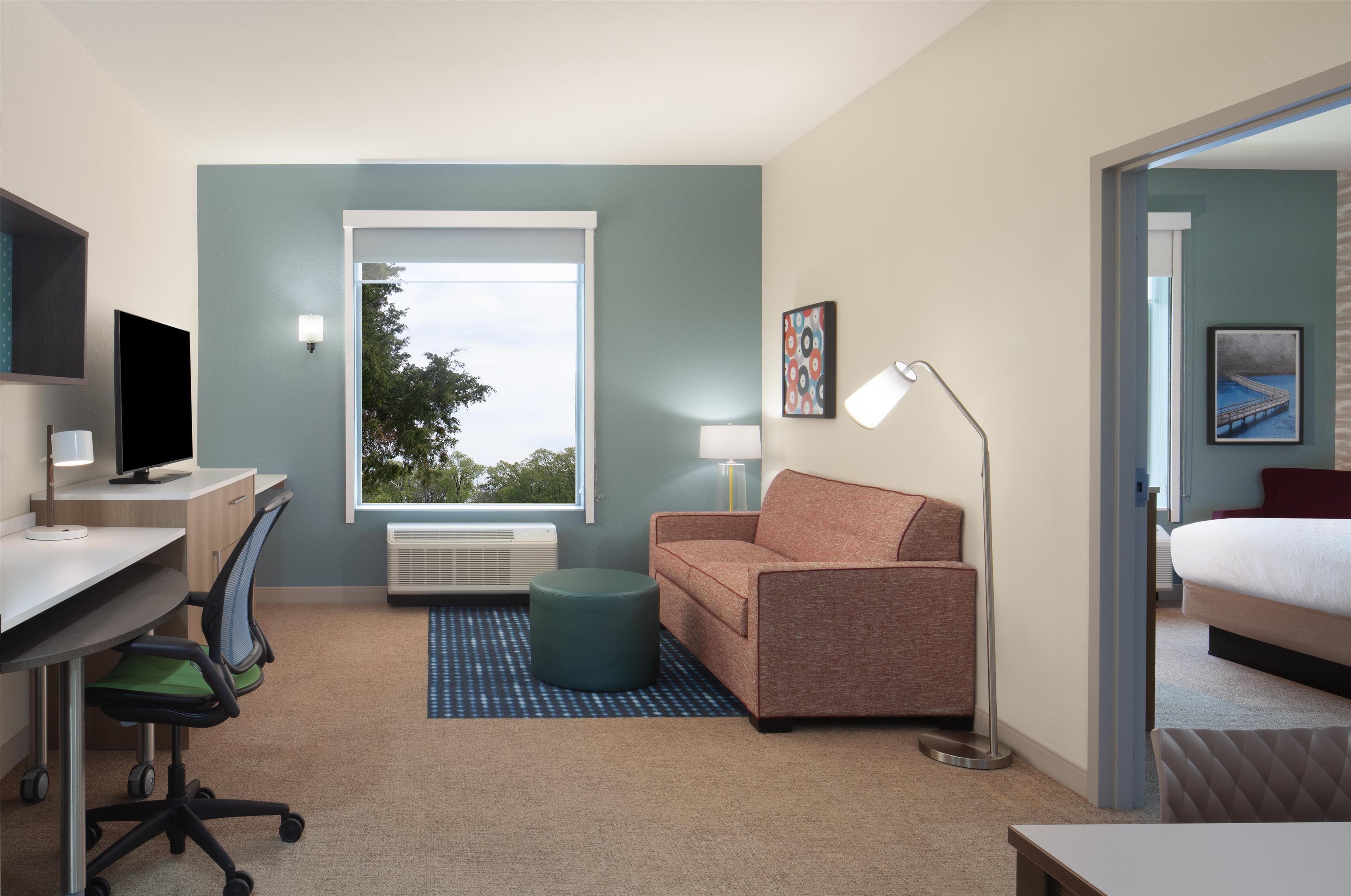 A modern hotel room with a desk, office chair, sofa, and a bed.