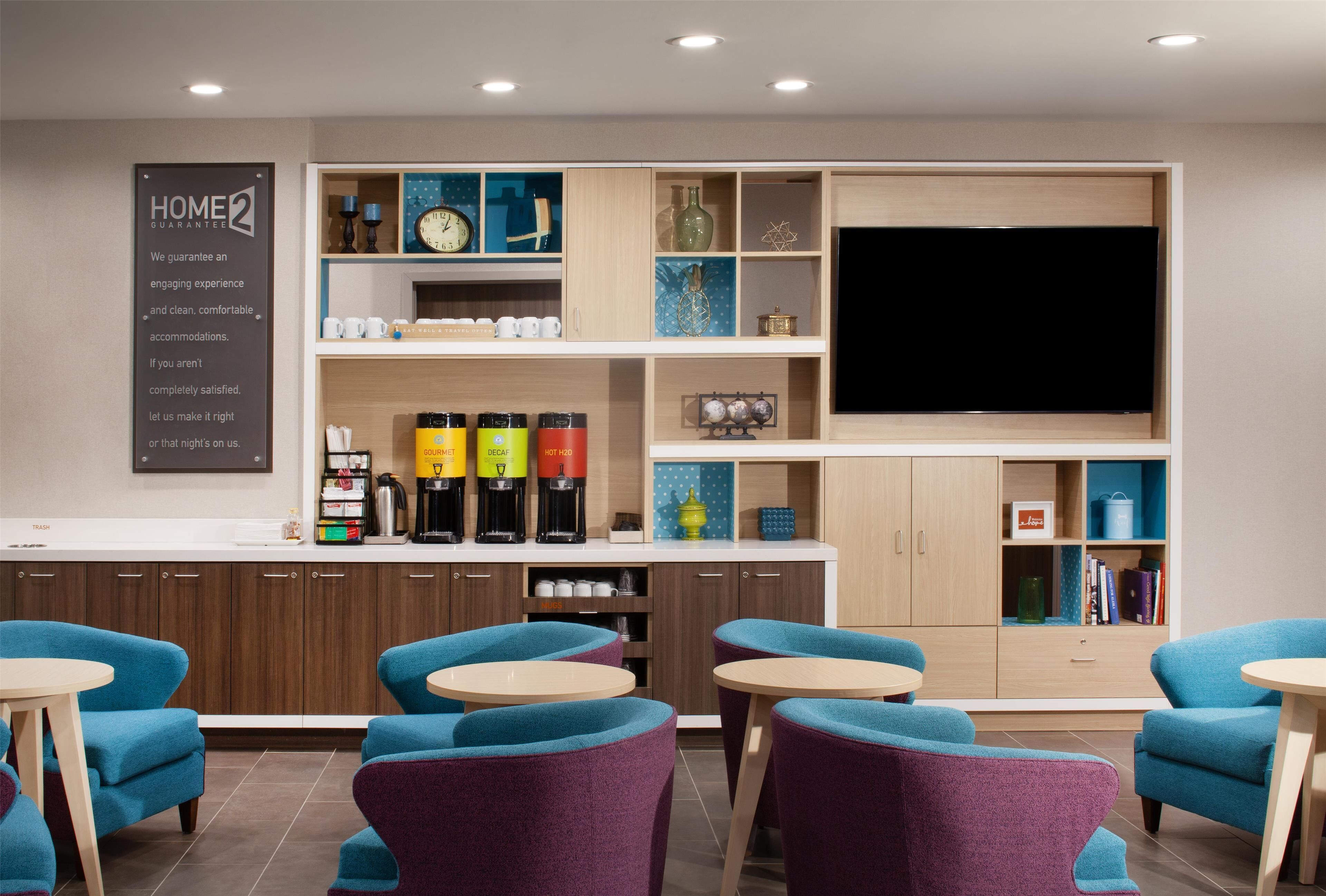 A hotel lobby with a coffee station, seating area, and a large flat-screen TV.
