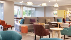 A modern lounge area with a sofa, chairs, and tables. - Home2 Suites By Hilton Jackson (Jackson)
