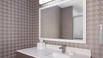 Un baño con papel tapiz estampado con diseño de piedritas, un lavamanos blanco con grifo plateado, un espejo sobre el lavamanos y una caja de pañuelos en la encimera.