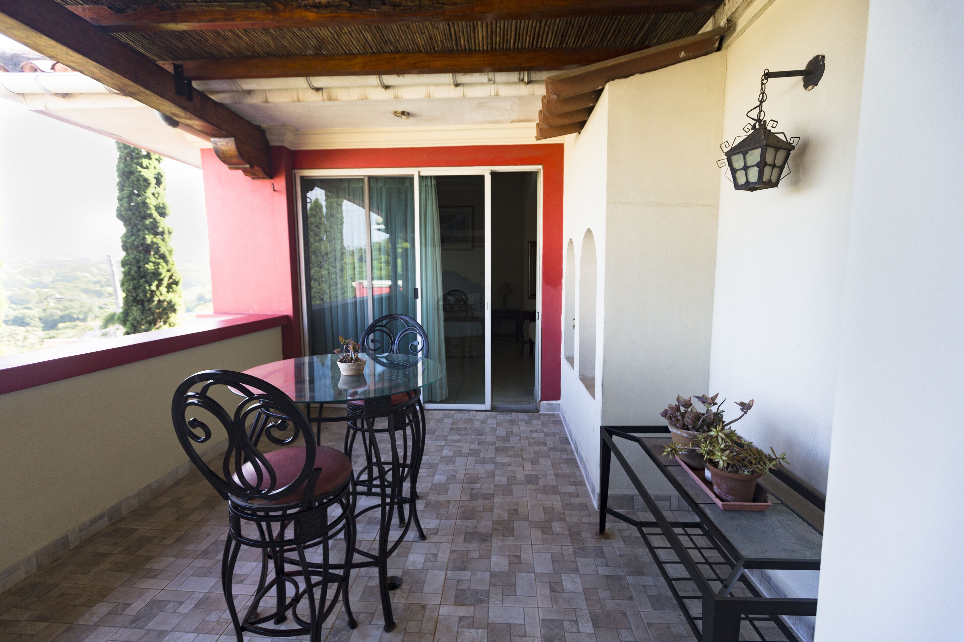 A balcony with a glass table and chairs, a hanging light fixture, and potted plants.