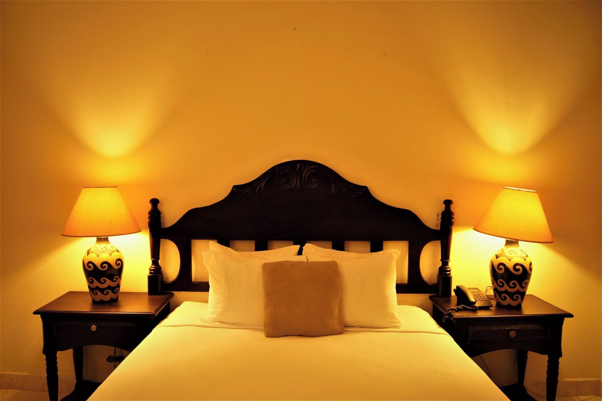 A hotel room with a bed, two bedside tables with lamps, and a headboard.