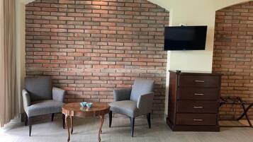 Una habitación con pared de ladrillo, dos sillas estampadas, una mesa de madera, un televisor colocado sobre la pared y un aparador de madera.