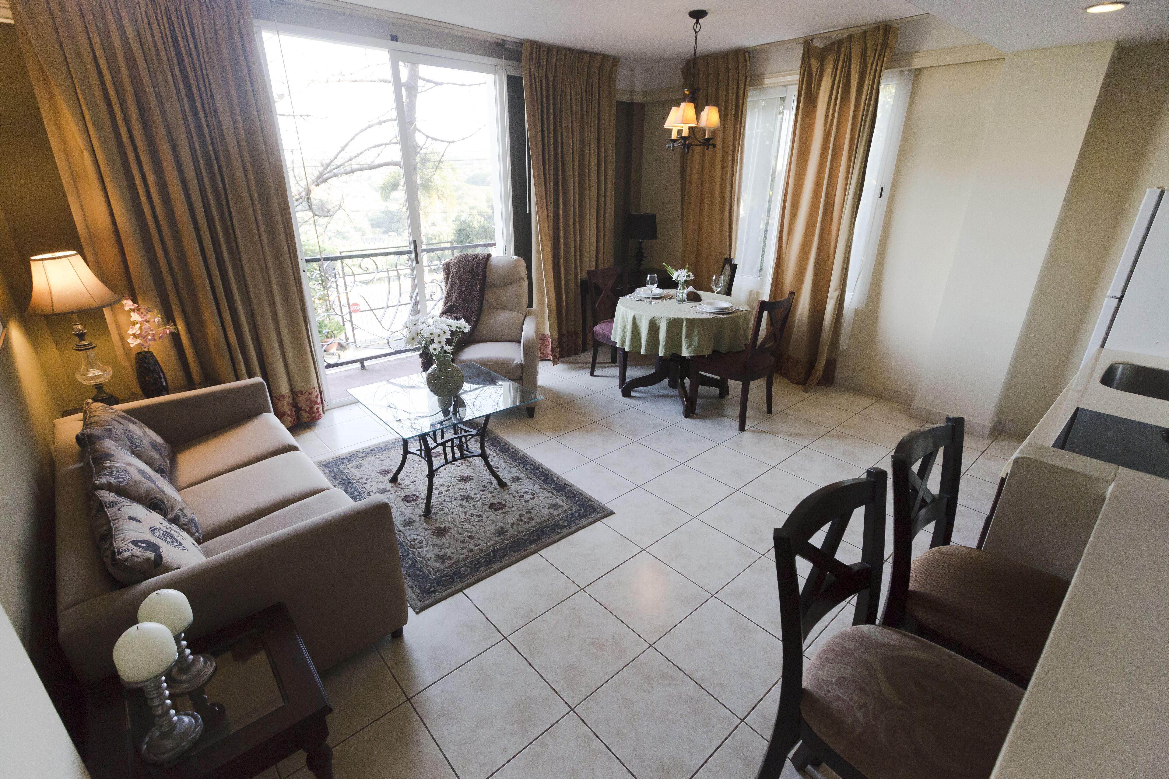 A spacious living area with a sofa, armchairs, a dining table with chairs, and a large window with curtains.