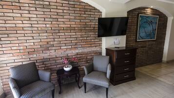 A living room with a brick wall, two patterned chairs, a small table with a vase, and a dark wooden cabinet.