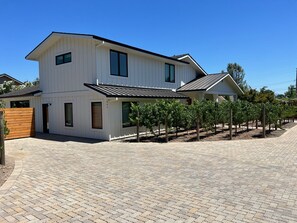 A two-story white house with a covered patio and a vineyard in the backyard.