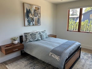 A bedroom with a bed, nightstands, a window with a view, and a painting on the wall.
