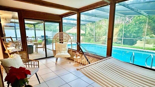 A sunlit room with a hammock, a pool view, and a seating area with a table and chairs.