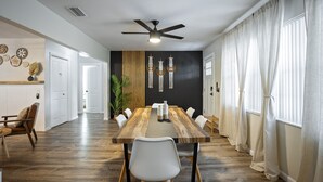 A modern dining area with a wooden table, white chairs, and a ceiling fan.
