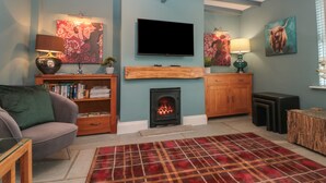 A living room with a fireplace, a flat-screen TV, and a plaid rug. - Stillwater Cottage (Beverley)