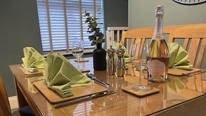 A dining table set with green napkins, cutlery, wine glasses, and a bottle of Prosecco. - Stillwater Cottage (Beverley)