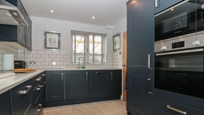 A modern kitchen with dark cabinetry, stainless steel appliances, and a tiled backsplash. - Stillwater Cottage (Beverley)