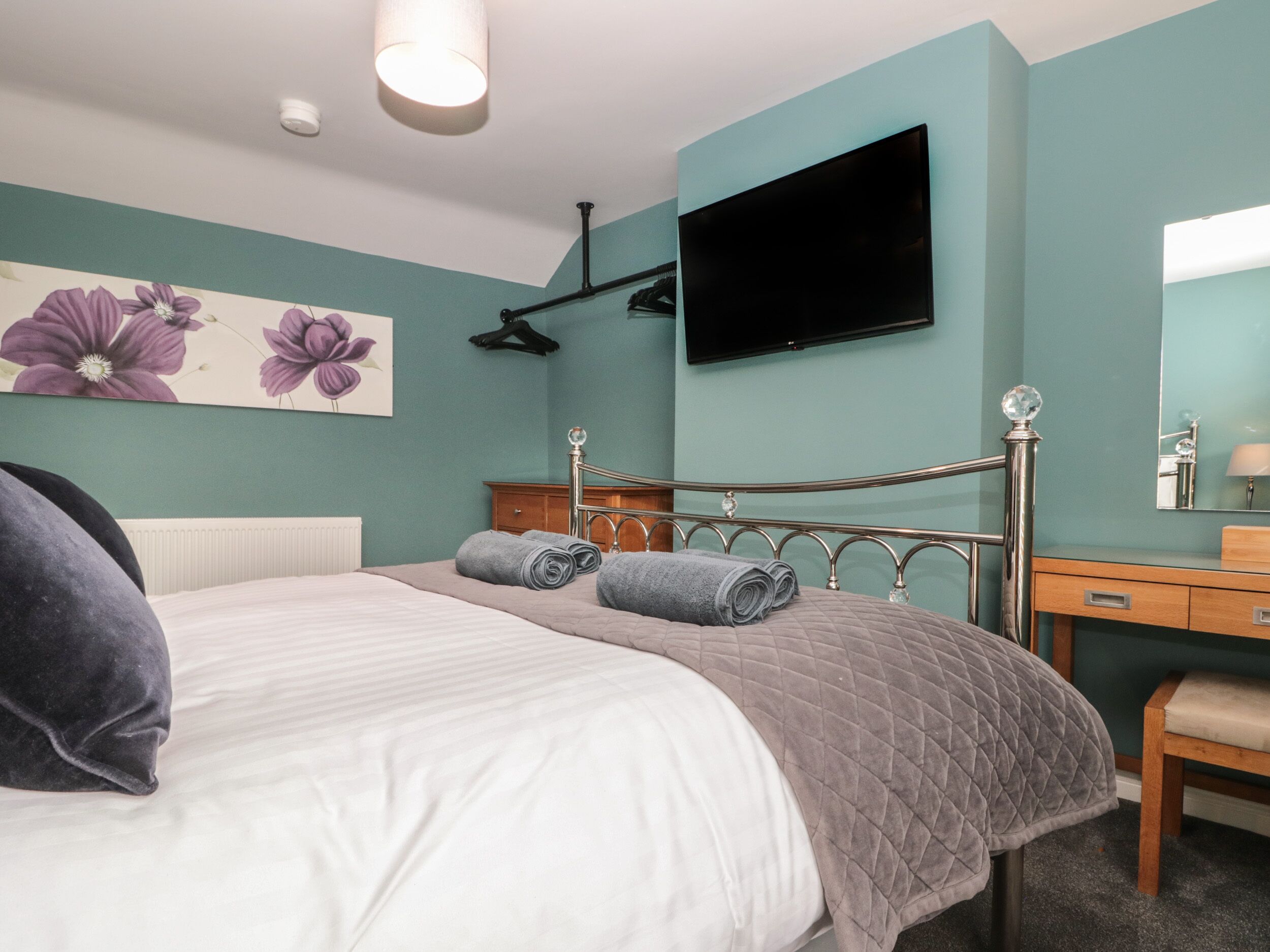 A bedroom with a bed, a dresser, a mirror, and a flat-screen TV mounted on the wall.