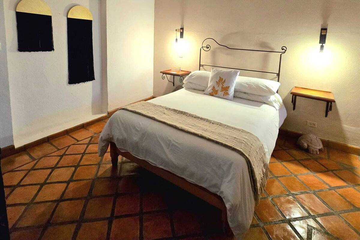 A bedroom with a bed, two wall-mounted lights, a small bedside table, and a tiled floor.