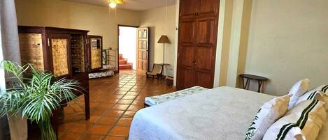 A bedroom with a large bed, a wooden wardrobe, a ceiling fan, and a potted plant.