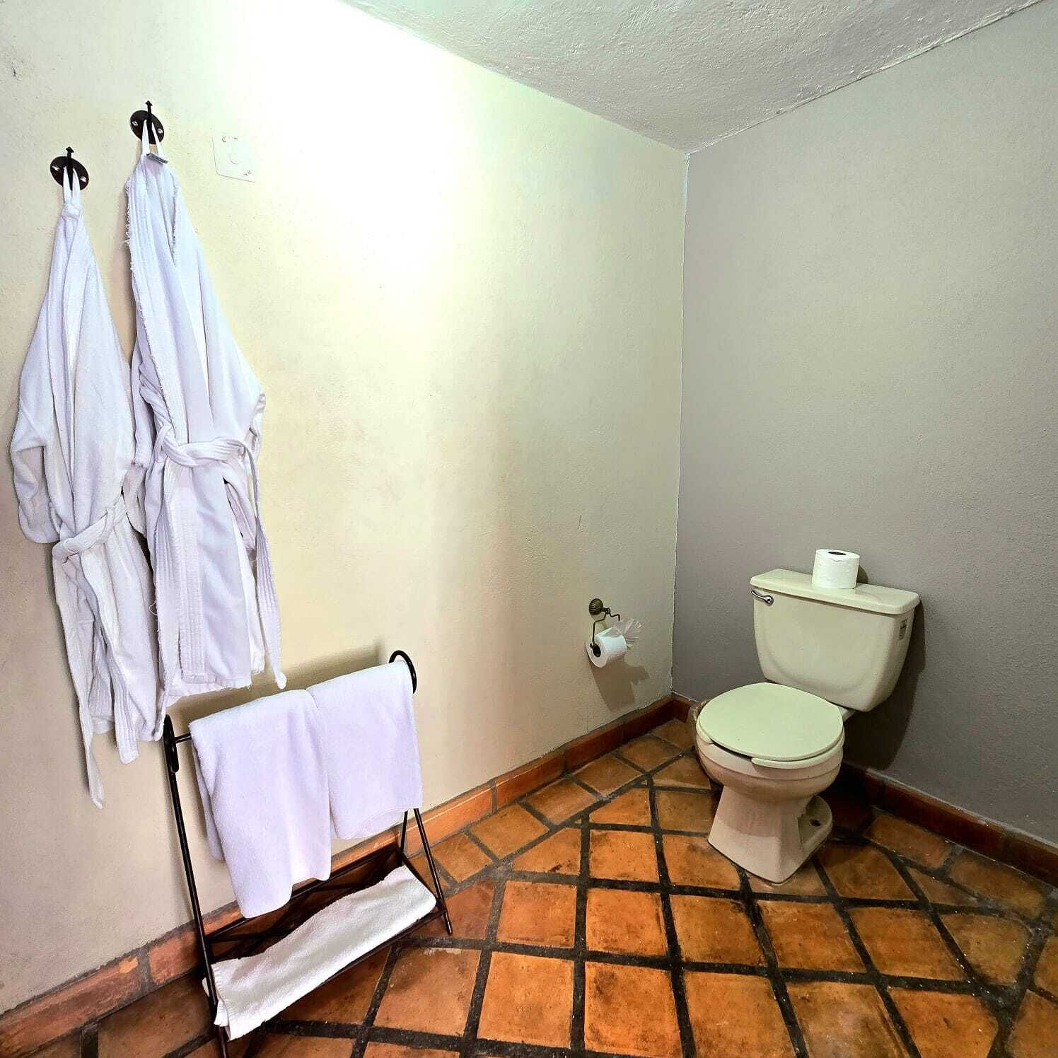 Ein Badezimmer mit Toilette, einem Handtuchhalter mit zwei weißen Handtüchern und einer Toilettenpapierhalterung.