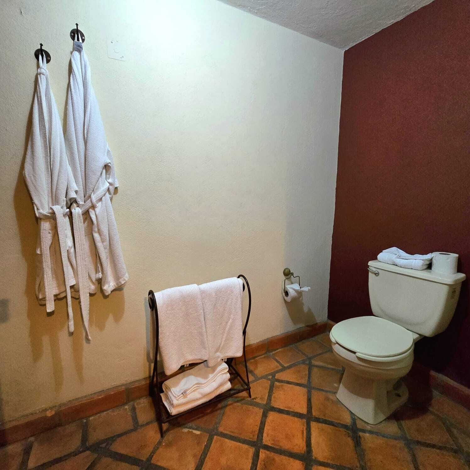 Ein Badezimmer mit Toilette, einem Handtuchhalter mit Handtüchern und einem Regal mit gefalteten Handtüchern.