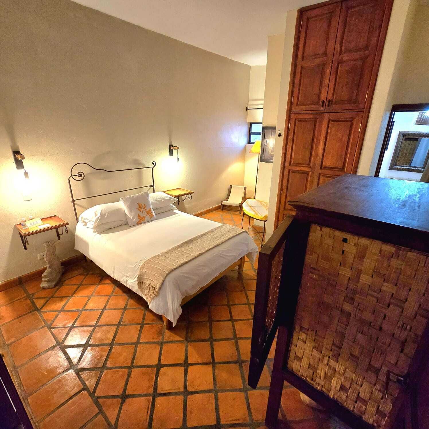 A room with a bed, bedside tables, a wooden cabinet, and a tiled floor.