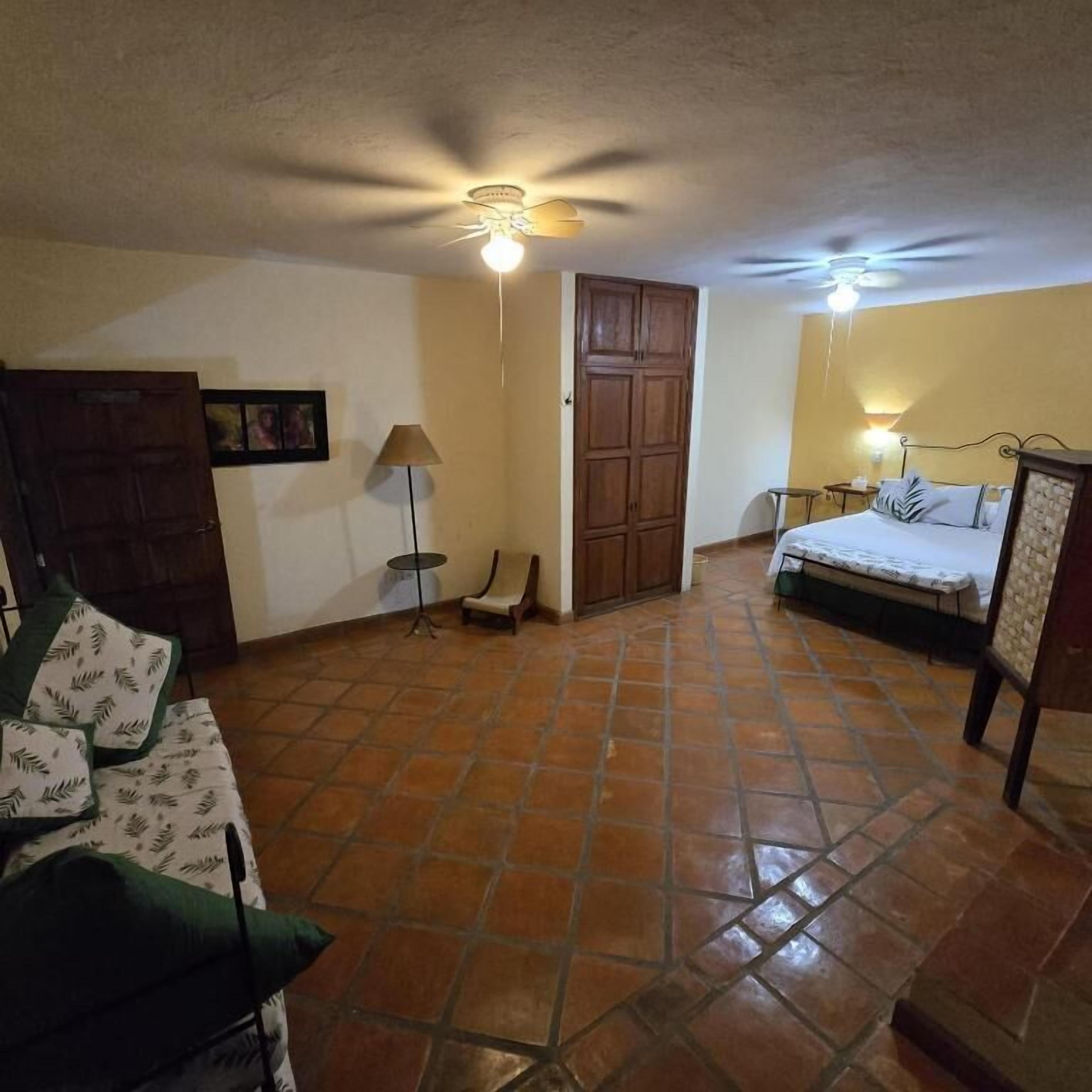 A bedroom with a bed, a chair, a wardrobe, a lamp, and a ceiling fan.