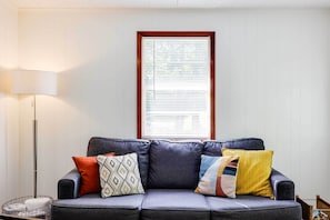 Ein graues Sofa mit gemusterten Kissen, eine Stehlampe und ein Fenster mit Jalousien.