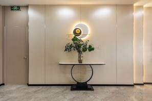 A reception area with a marble floor, a reception desk with a vase of flowers, and a wall-mounted light fixture. - Elong ME Hotel (Binhai High-Speed Railway Station) (Tianjin)