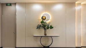 A modern lobby with a marble floor, a wall-mounted circular light fixture, and a vase with green plants on a console table. - Elong ME Hotel (Binhai High-Speed Railway Station) (Tianjin)