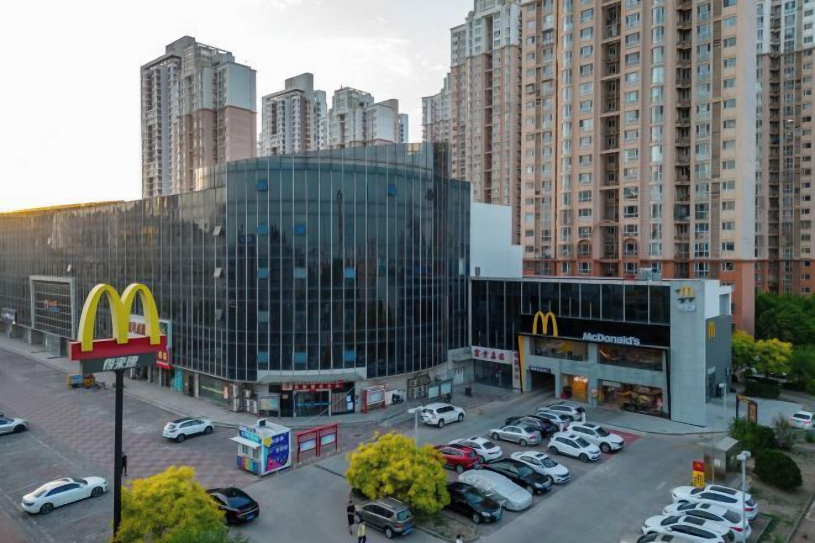 A McDonald's restaurant with a glass facade, surrounded by tall residential buildings.
