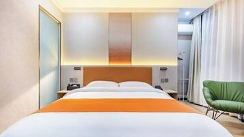 A hotel room with a large bed, a nightstand, a green chair, and a view of the city.