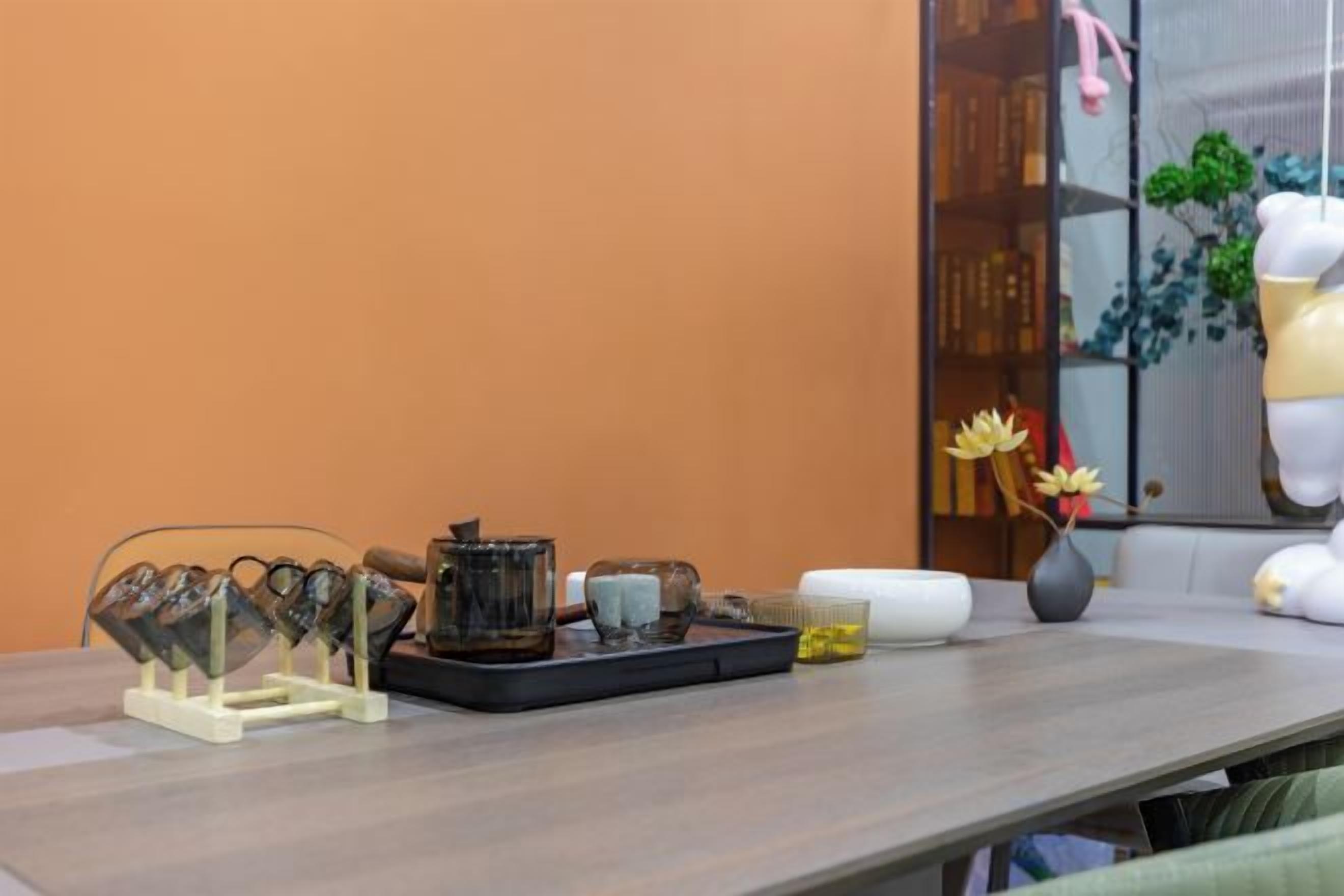 A table with a tray of items, a vase with flowers, and a bookshelf with books and decorative items.