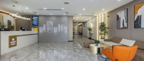 A hotel lobby with a reception desk, seating area, and a digital display.