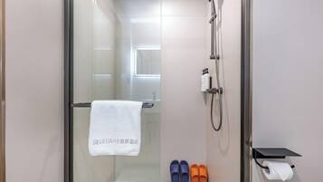 A modern bathroom with a glass shower enclosure, a towel hanging on the door, and a pair of slippers on the floor.