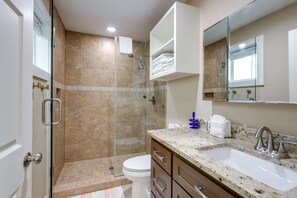 Ein Badezimmer mit Duschkabine, Toilette in Weiß, Waschbecken mit Marmorplatte und Spiegel über dem Waschbecken.