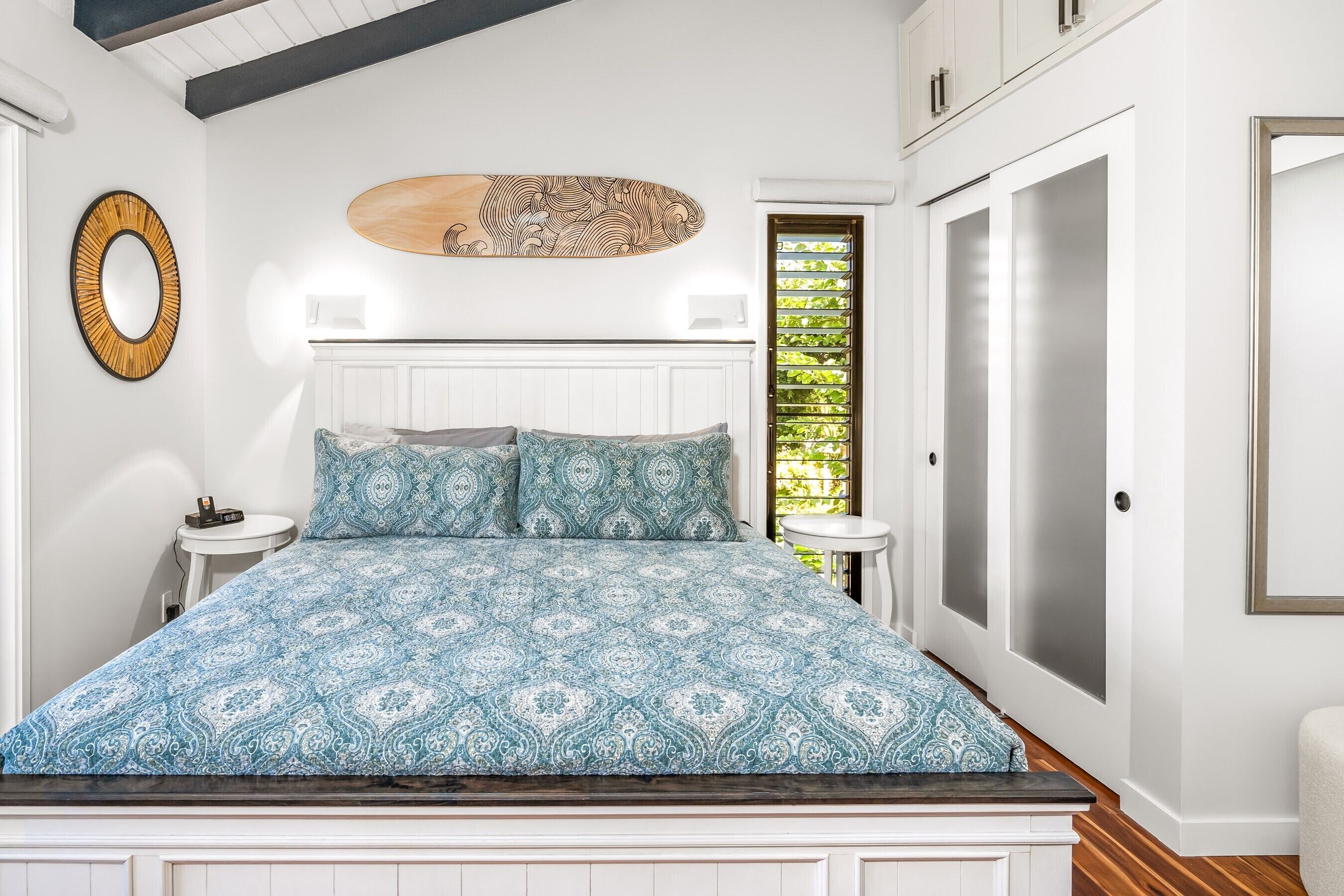 A bedroom with a patterned bedspread, a round mirror, and a wall-mounted artwork.