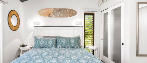 A bedroom with a patterned bedspread, a round mirror, and a wall-mounted artwork.