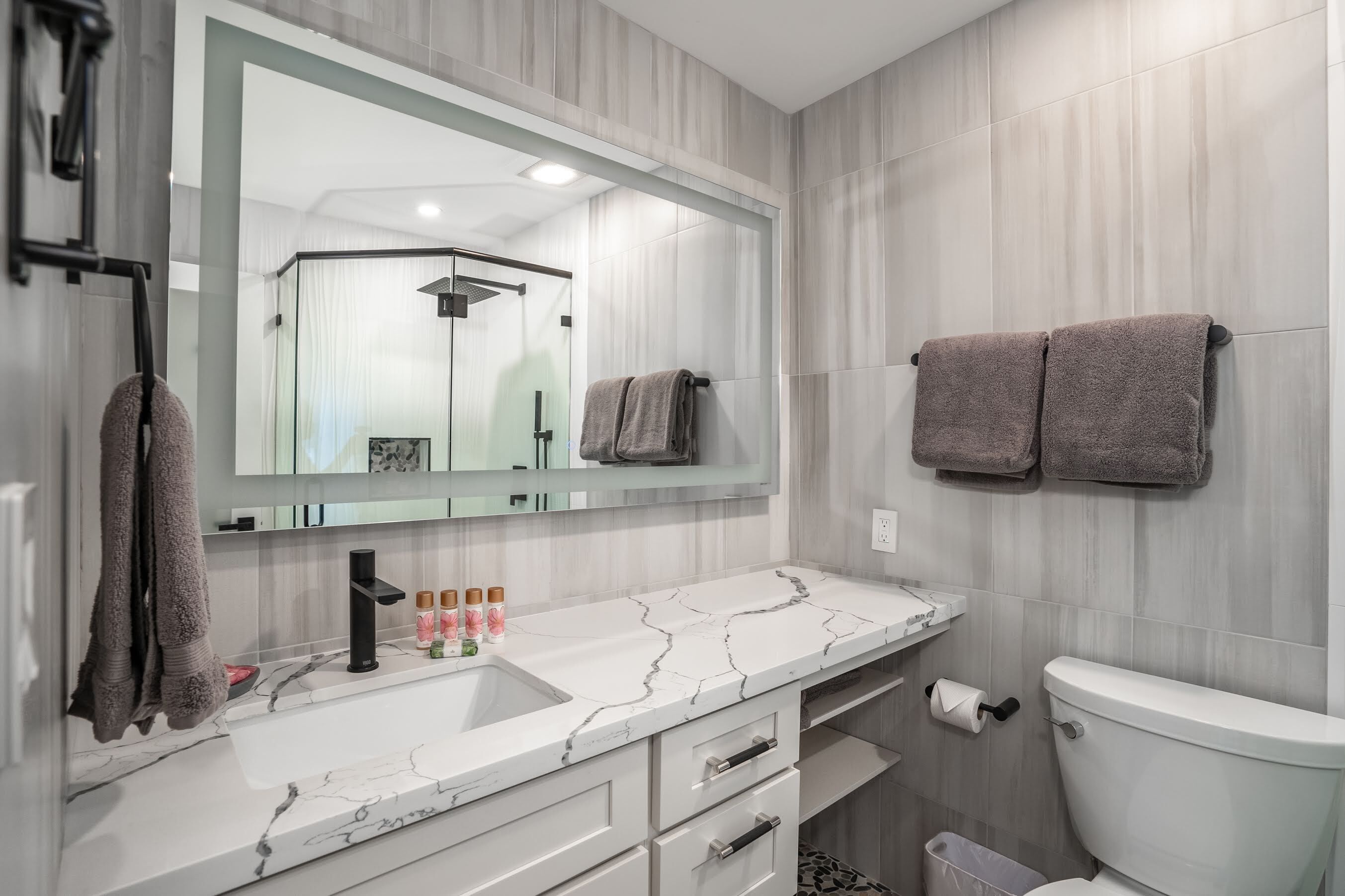 A modern bathroom with a white marble sink, a large mirror, and a toilet.