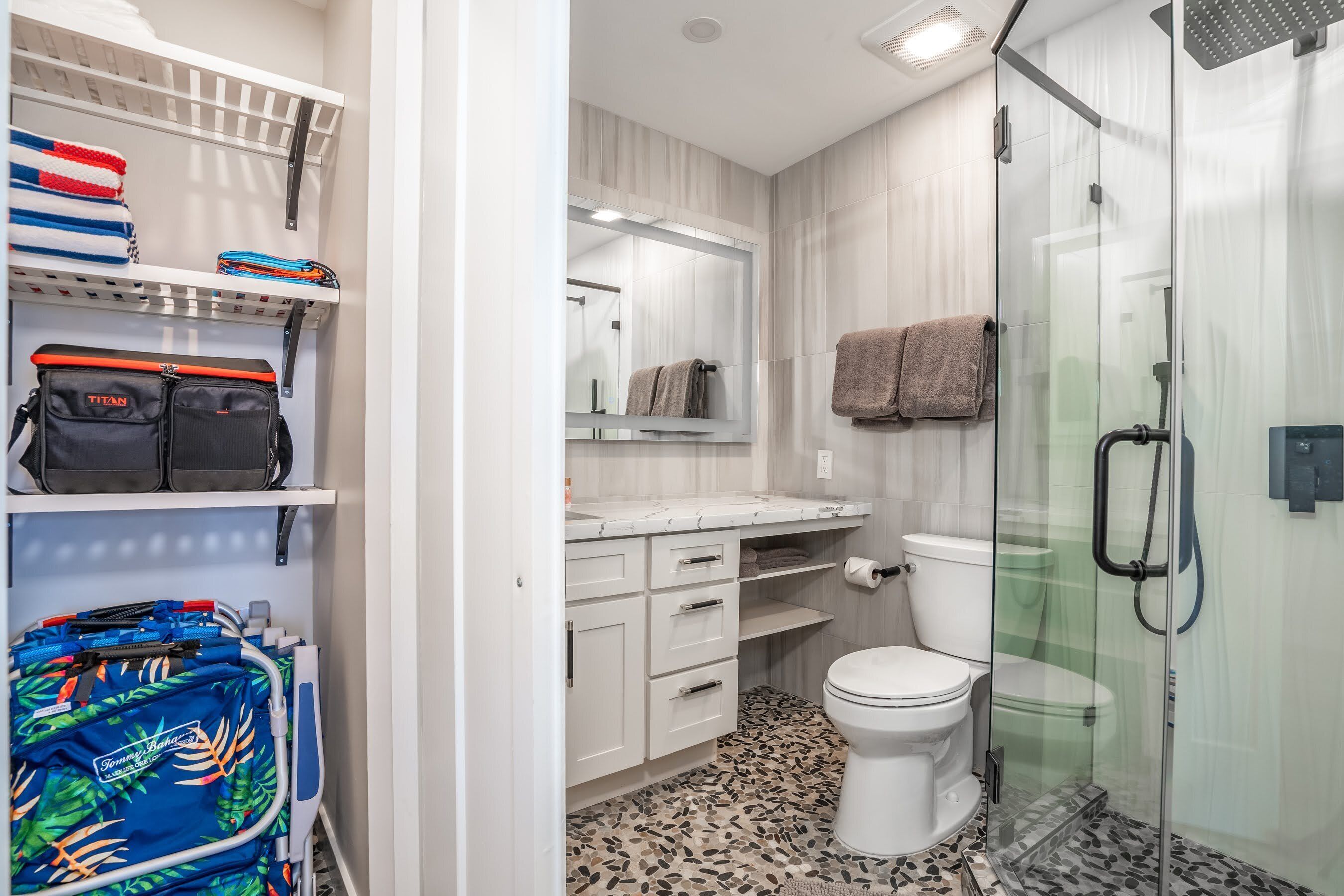 A modern bathroom with a toilet, shower, and a glass-enclosed shower stall. There is a vanity with a mirror and a towel rack.