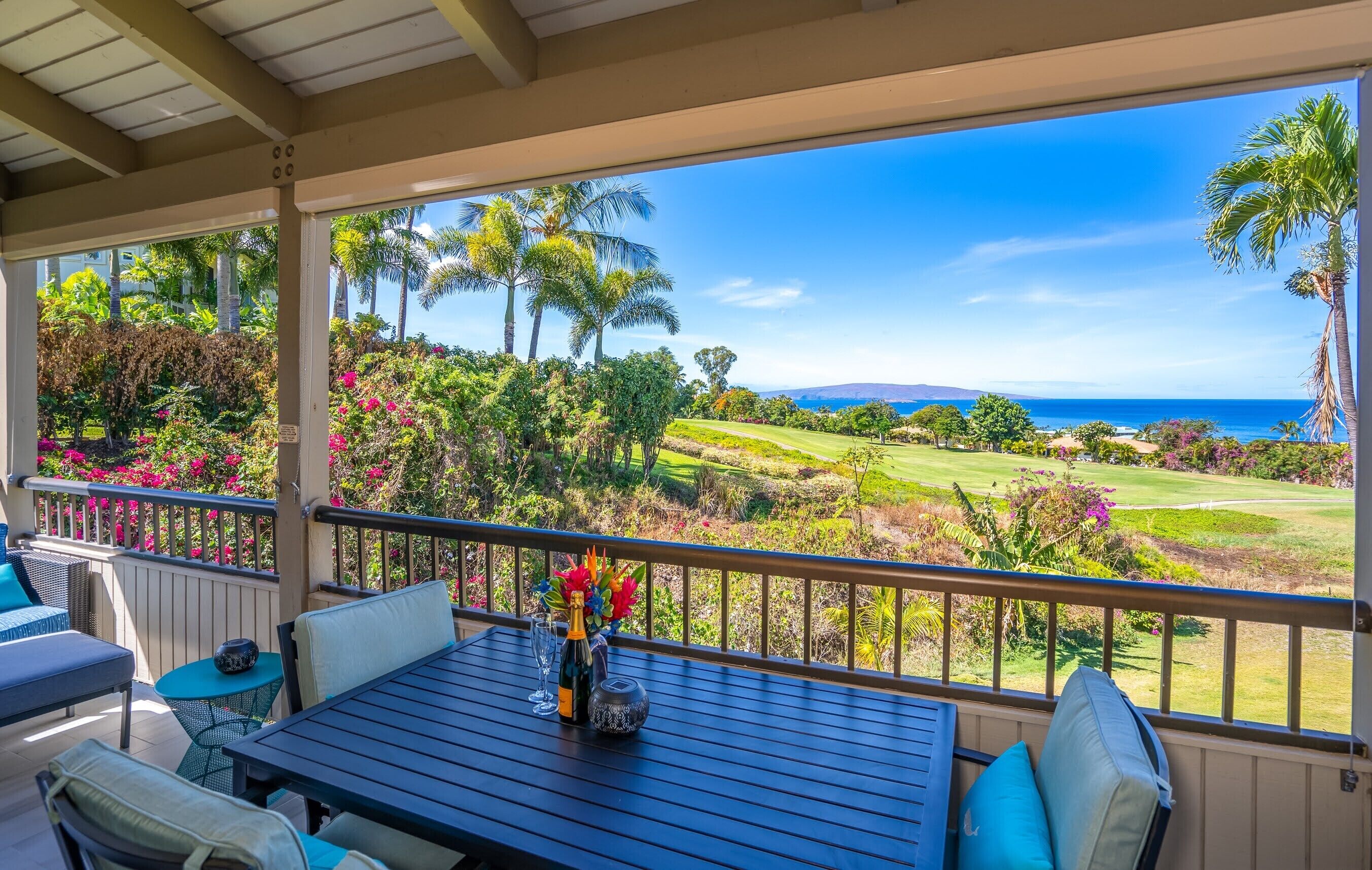 A covered outdoor seating area with a table, chairs, and a view of a golf course and ocean.