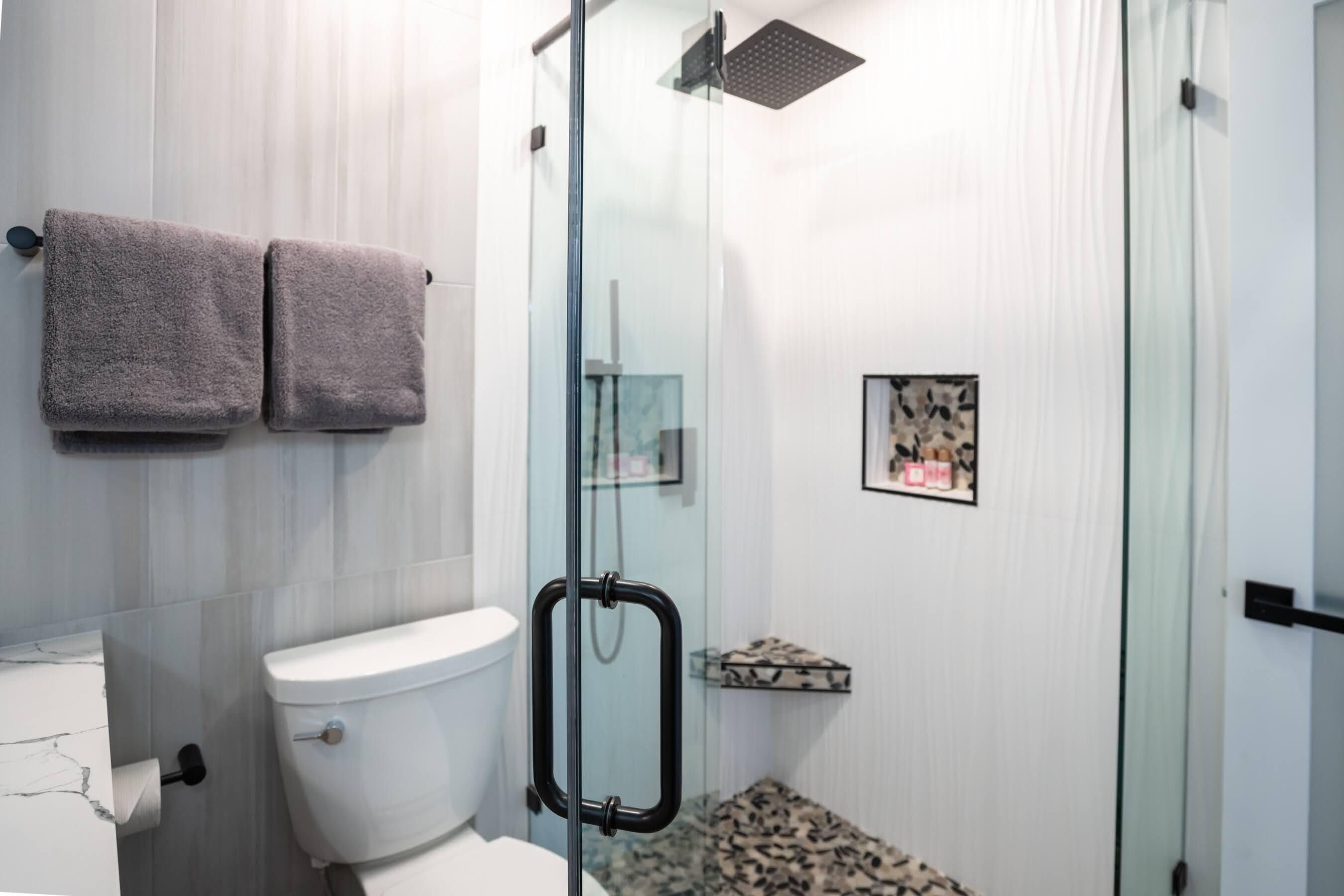 A modern bathroom with a glass shower enclosure, a toilet, and a marble-tiled vanity.