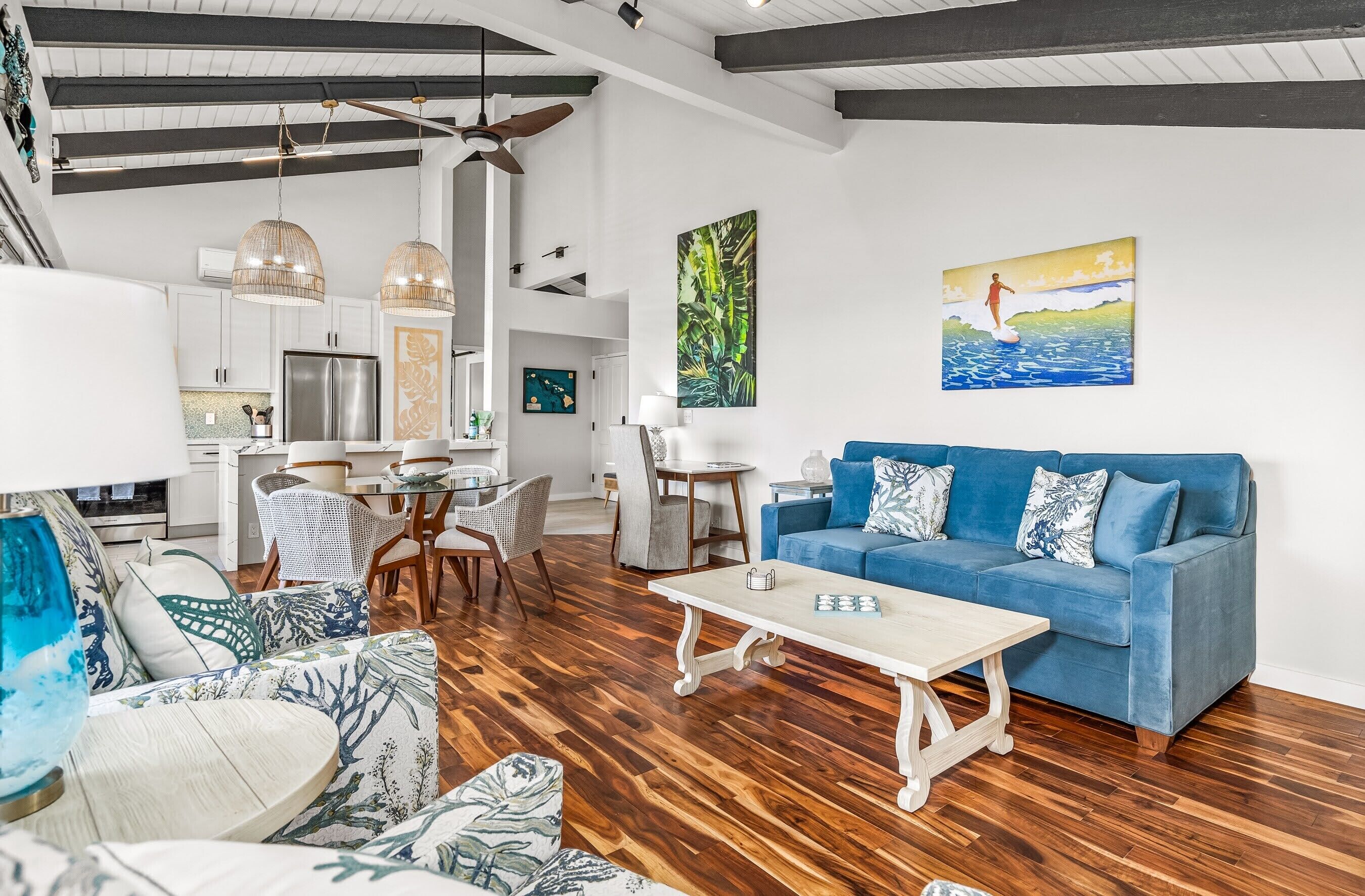 Un salón amplio con un sofá azul, piso de madera y un comedor con mesa y sillas.