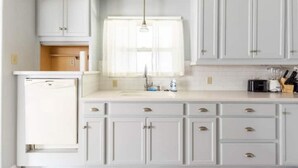 A kitchen with white cabinets, a built-in dishwasher, and a window with sheer curtains. - Clean&Cozy 3 bedroom 2 bath home No cleaning fees
 (Fresno)