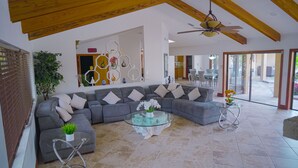 A spacious living area with a large gray sectional sofa, a glass coffee table, and a ceiling fan.