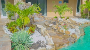 A landscaped pool area with tropical plants, a small waterfall, and a stone border.