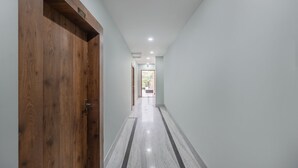 A hallway with a wooden door on the left, a tiled floor, and a view into a room with a balcony. - Itsy Hotels Greenland Jungle View (Bhubaneshwar)