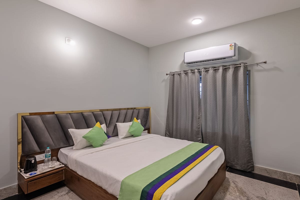 A hotel room with a bed, a nightstand, an air conditioning unit, and a curtain.
